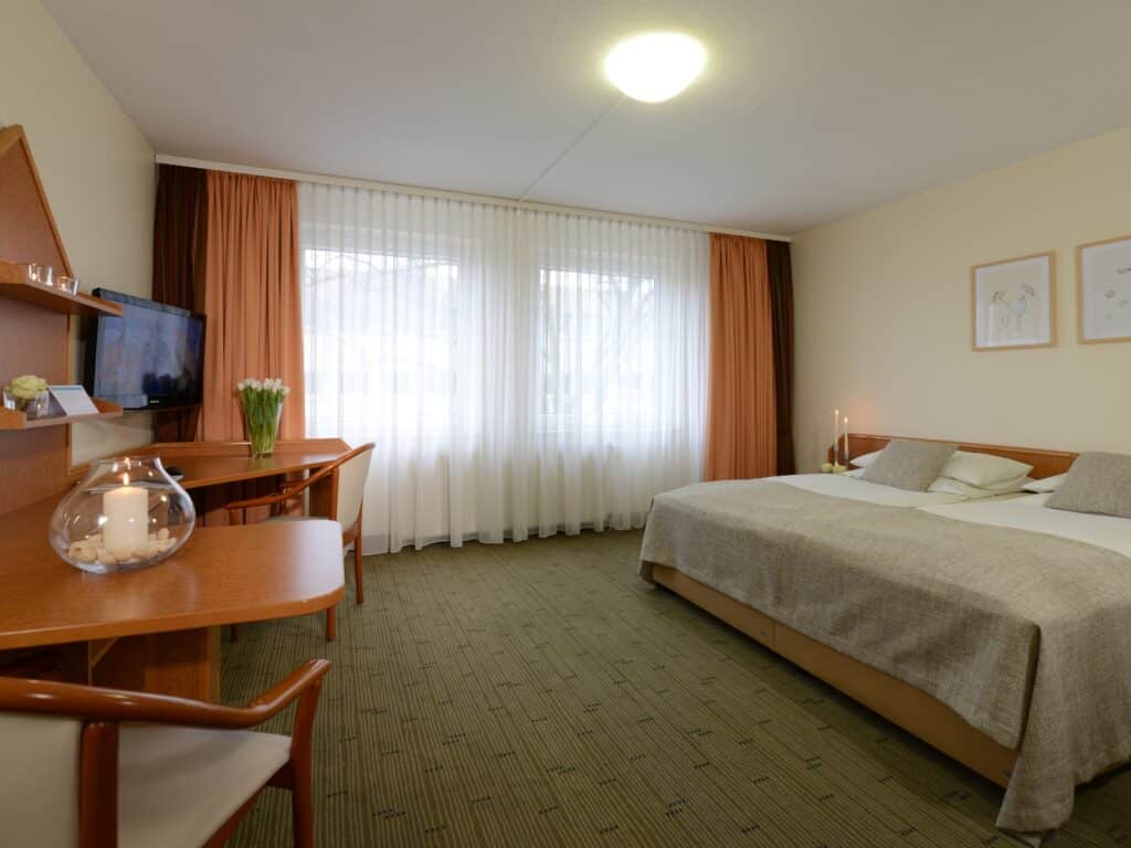 Komfortzimmer im Hotel Residenz Oberhausen. Blick aufs Bett an der rechten Seite und links auf einen Tisch mit Stühlen. Mit Teppichboden grünlich