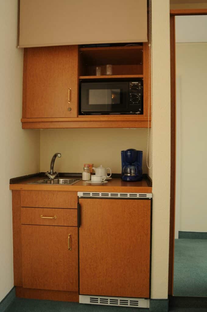 Kitchenette im Komfortzimmer Hotel residenz Oberhausen. Mit Blick auf Küche mit Spüle und Kühlschrank, Hängeschrank. Hellbraun