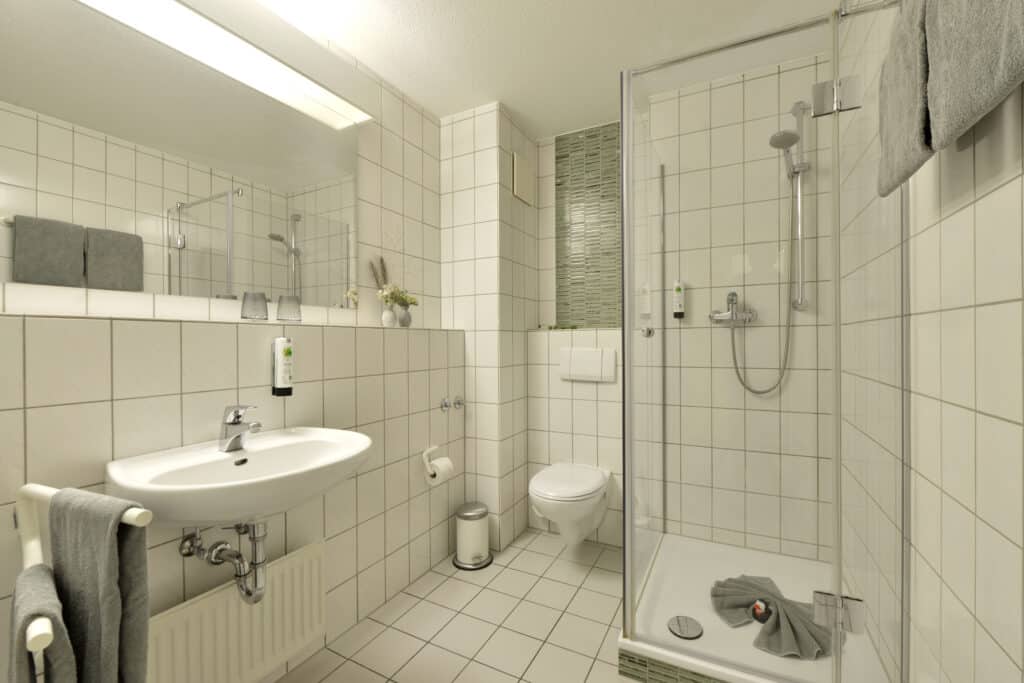 Badezimmer Komfort im Hotel Residenz Oberhausen. weiß gefließt mit Blick auf Waschbecken und Dusche