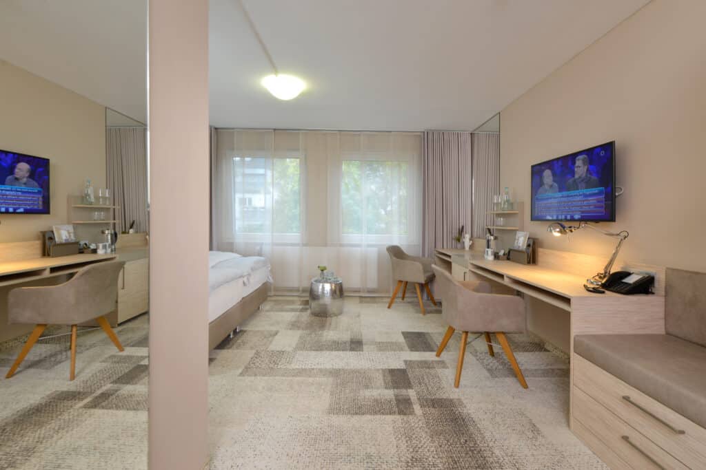 Superiorzimmer Hotel Residenz Oberhausen mit Blick in das Zimmer. Links sieht man einen Teil vom Bett, rechts die Schreibtischwand mit TV. in beige Tönen gehalten