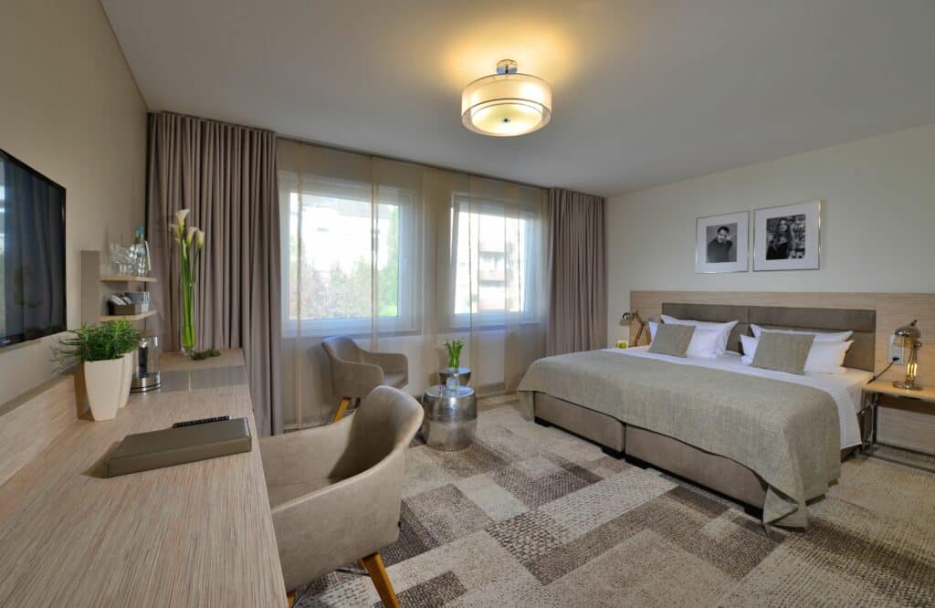 Superior Zimmer im Hotel Residenz Oberhausen mit Blick auf das Bett am rechten Rand und links Schreibtischwand mit Stuhl. In hellen braun und beige Tönen.